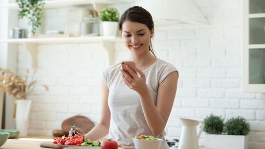 Frau schaut auf Handy, vor ihr ein gedeckter Tisch © Shutterstock