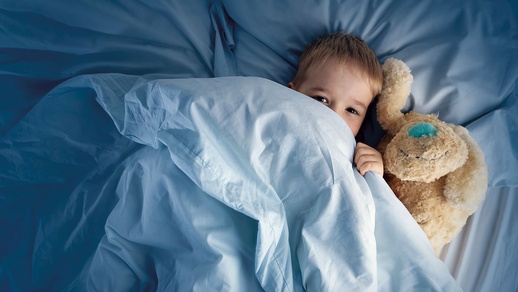 Kind schläft in einem Bett, unter der Decke mit seinem Kuscheltier © iStock