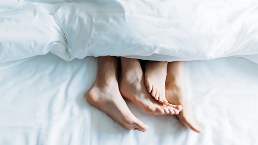 Ein Paar liegt im Bett. Man sieht nur die Füße, die unter der Decke herausschauen. © Shutterstock