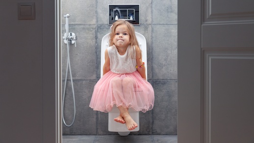Kleines Mädchen in rosa Kleid sitzt auf der Toilette und sieht ein wenig unglücklich aus. © Shutterstock