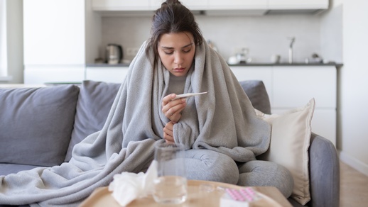 Eine Frau betrachtet ein Fieberthermometer. © Shutterstock