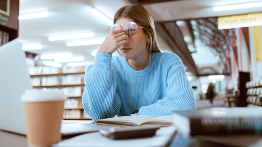 Eine junge Frau sitzt vor Lernunterlagen und greift sich an den Kopf.  © iStock