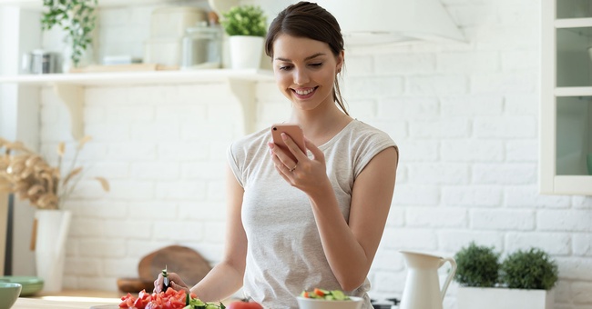 Frau schaut auf Handy, vor ihr ein gedeckter Tisch © Shutterstock