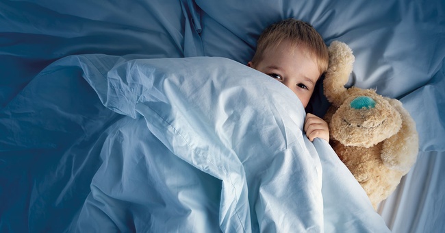 Kind schl&auml;ft in einem Bett, unter der Decke mit seinem Kuscheltier &copy; iStock