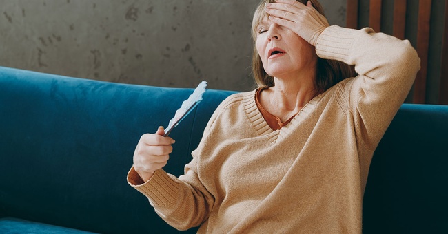 Frau sitzt auf dem Sofa und kämpft mit der Hitze. © Shutterstock
