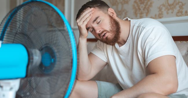 Mann leidet unter Hitze und kühlt sich mit Ventilator © Shutterstock