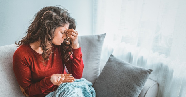 Eine Frau hat Kopfschmerzen und hält eine Tablette in der Hand. © Shutterstock