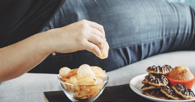 Eine Frau liegt auf dem Sofa und ist Chips. © Shutterstock