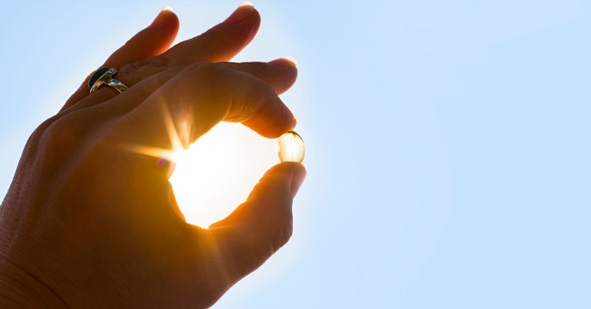 Eine Frau hält eine Vitamin-D-Kapsel ins Licht. © Shutterstock
