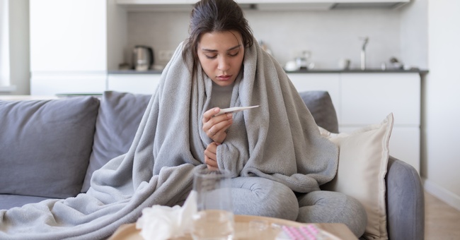 Eine Frau betrachtet ein Fieberthermometer. © Shutterstock