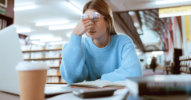 Eine junge Frau sitzt vor Lernunterlagen und greift sich an den Kopf.  © iStock