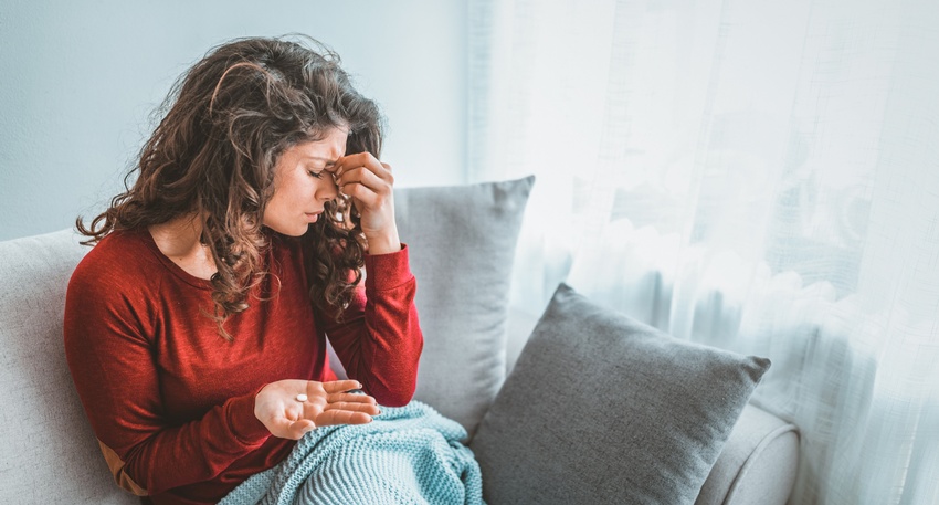 Eine Frau hat Kopfschmerzen und hält eine Tablette in der Hand. © Shutterstock