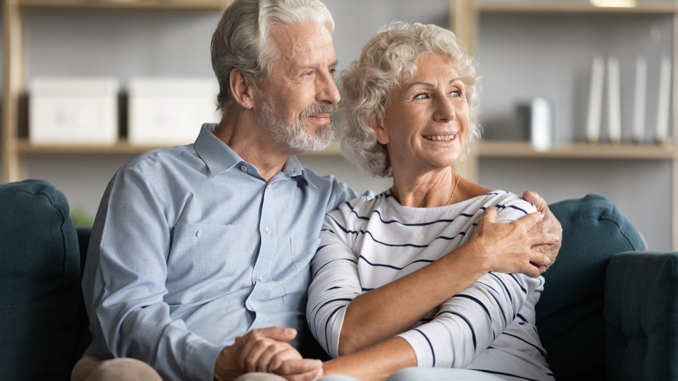Ein Seniorenpaar sitzt auf dem Sofa und lächelt. © Shutterstock